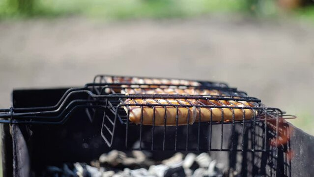 Close-up of sausages that are cooked over coals on the grill. The guy turns over the grill with sausages
