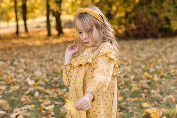 A beautiful little blonde girl is walking in an autumn park.