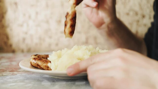 A man is sitting at a table and eating mashed potatoes with sausages. Close-up shooting from the side