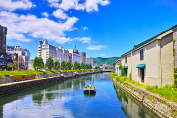 新緑の北海道小樽市、浅草橋街園から見る快晴の小樽運河の倉庫群と運河クルーズ船
