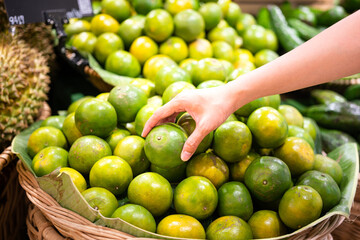 Action of human hand is picking up a piece of green orange or tangerine from the stall at supermarket. Buying and eating diet food concept photo, selective focus at hand.