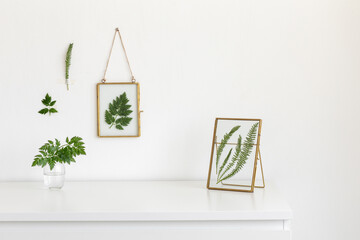 Composition of golden glass photo frames with green leaves on white table. Stylish home decor. Modern interior design.