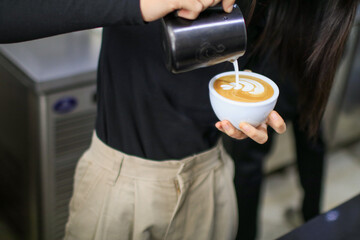 Coffee Latte art by barista pouring steamed milk into coffee cup in cafe. 