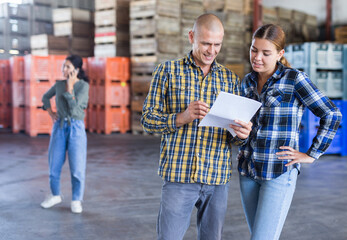 Man having conversation with young woman about documentation in warehouse. Those female colleague standing behind.