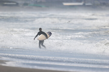 湘南の荒れた海でサーフボードを持ってビーチを歩く男性