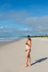 Woman in bikini walking on beach sand against blue sky.