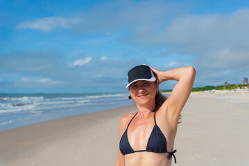 Portrait of woman in black bikini against beach and blue sky.