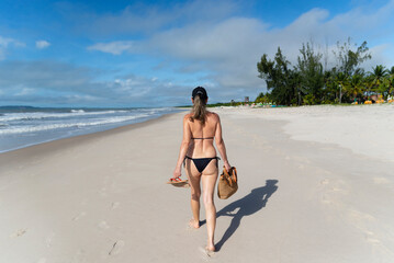 Woman in bikini walking on beach sand against blue sky.