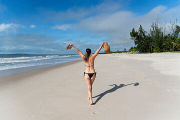 Woman in bikini walking on beach sand against blue sky.