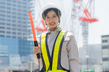 誘導棒を持ち笑顔でカメラを見る工事現場で働く女性