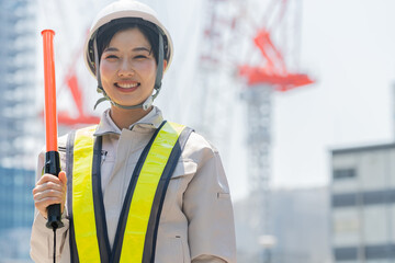 誘導棒を持ち笑顔でカメラを見る工事現場で働く女性