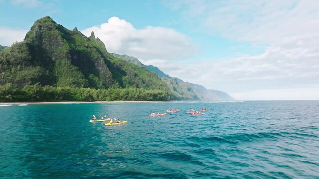 Summer activity, Napali coast kayak tour Hawaii island. Aerial drone view following kayaks, paddling along breathtaking beautiful green tropical mountain range at early morning sunrise on Kauai island