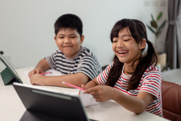Obraz premium Asian boys and girls enjoy online learning by taking notes and using tablets at home.