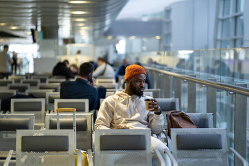 Young African American traveler man drinking coffee and eating sandwich while waiting for flying at...