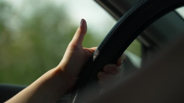 Woman's hand taps thumb against steering wheel while driving a car. Slow motion. Close up.