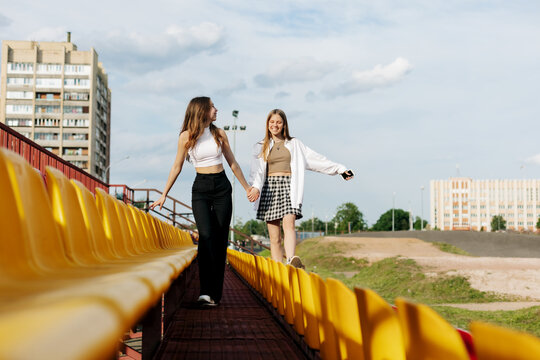 Two teenage girls walk together through the stands of the school stadium, talking, holding hands, best friends return home after training