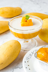 Mango pudding topping with fresh ripe mango cut dice shape and mint in glass bowl on a marble table. cake in cafe or bakery shop.