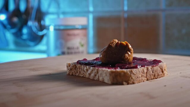 Putting Spoonful Of Peanut Butter Onto Whole Grain Bread With Fruit Jelly. close up