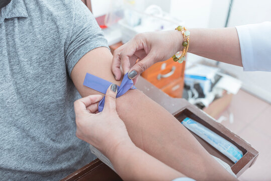 A nurse or phlebotomist tying a rubber IV Tourniquet placed above the elbow. Venipuncture for blood testing or hematology analysis.