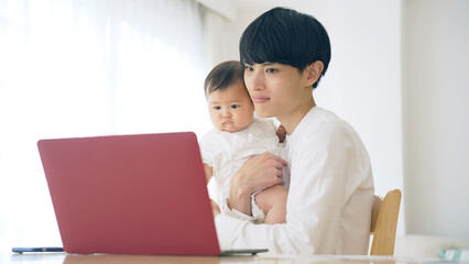 赤ちゃんを抱っこしながら自宅で仕事する男性