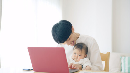 赤ちゃんを抱っこしながら自宅で仕事する男性