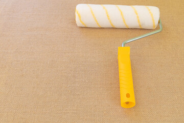 A roller with a yellow handle on a rustic fabric background