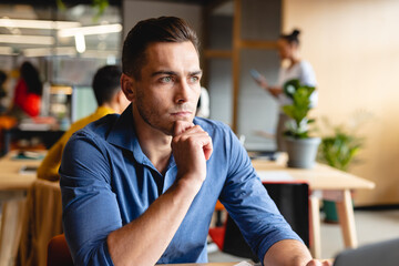 Thoughtful creative caucasian young businessman sitting with hand on chin in office