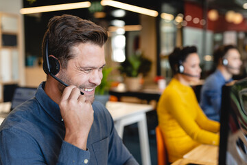 Smiling caucasian male customer service executive talking through headset in office