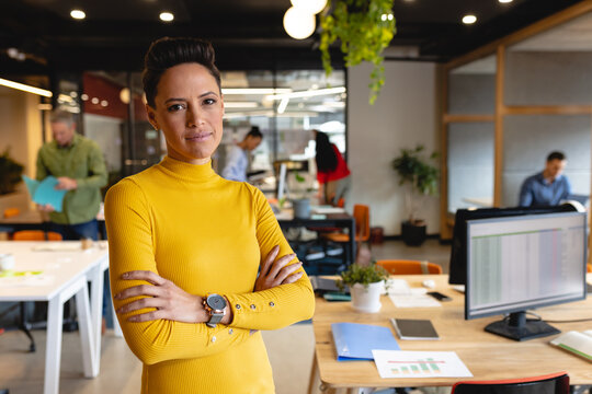 Portrait of confident young biracial businesswoman standing with arms crossed in creative office - Powered by Adobe