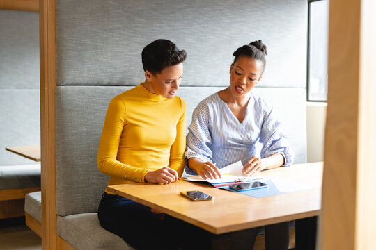 Multiracial businesswomen discussing over document in creative office