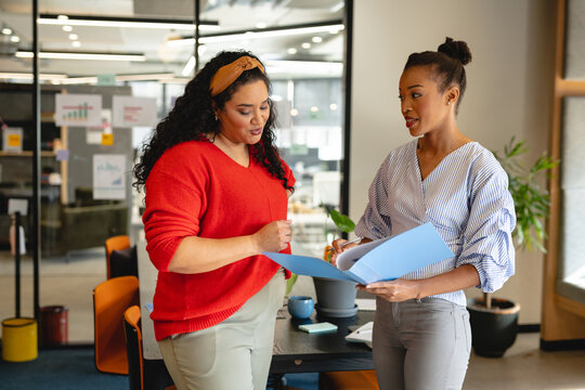 Multiracial businesswomen discussing over file while standing in creative office