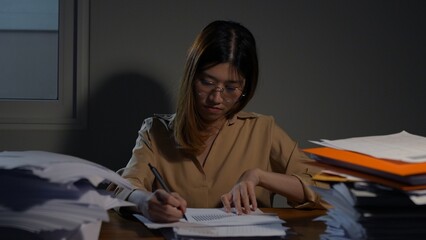 Asian businesswoman or freelancer working hard at the night looking the laptop digital tablet and document in workplace at late overtime deadline, Stressed busy and exhausted of work at home.