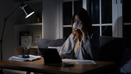 Asian businesswoman or freelancer working hard at the night looking the laptop digital tablet and...