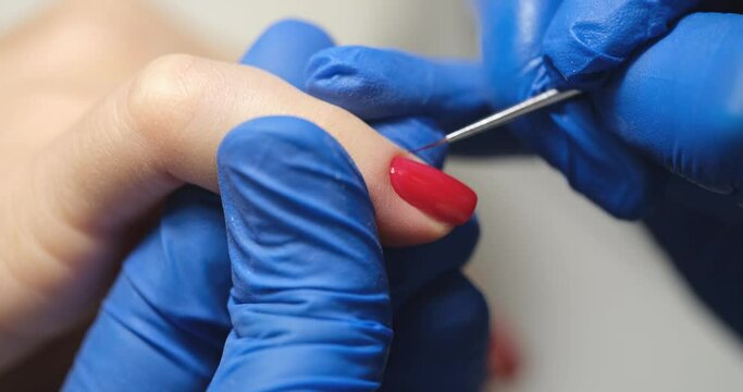 Manicurist paints client nails with bright red polish in salon closeup