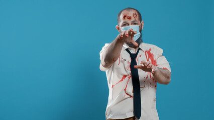 Mindless office zombie with covid protection mask and bloody wounds standing on blue background....