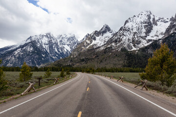 Fototapeta premium Scenic Road and Snowy Mountains in American Landscape. Spring Season. Grand Teton National Park. Wyoming, United States. Nature Background.