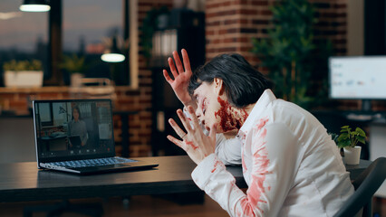 Creepy angry zombie in online video conference with asian colleague. Brain-eating walking dead...