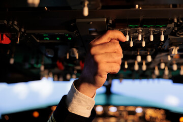 Man captain pushing control buttons on dashboard panel command to fly airplane jet from cabin. Male airliner using power switch navigation and windscreen, international airways.