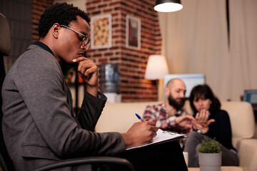 Frustrated therapist taking notes on paper at couple therapy session with married partners, having relationship conflict and difficulties. Trying to solve problems with psychology advice.