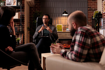 Psychotherapist talking to couple with marriage problems, trying to solve conflict and give support. Psychoanalysis counseling with relationship issues, professional advice in office.