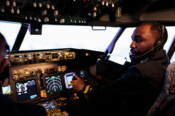 African american aviator flying plane jet in teamwork with captain, using dashboard command and...