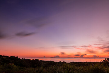 Fototapeta na wymiar Tranquil dawn by the sea, lilac sky, clouds in motion blur, island on the horizon.