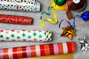 Different colorful wrapping paper rolls, gift bows and ribbons on grey table, flat lay - obrazy, fototapety, plakaty