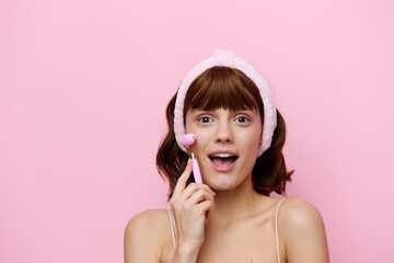 horizontal beauty photo of a funny, attractive woman with short hair, tucked behind a soft rim and smiling pleasantly while doing a facial massage with a pink roller