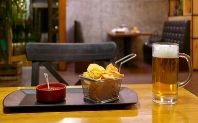 A basket of potato chips and dip with a glass of chilled draft beer on the wooden table
