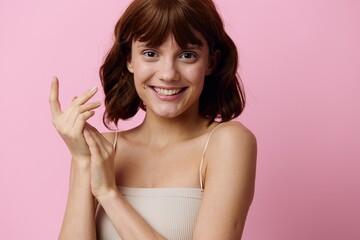 a sweet, elegant young woman stands on a pink background, happily smiling, posing with her hands in relaxed gestures. Horizontal studio photography with empty space