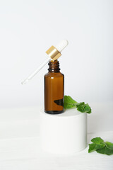 Mock up glass dropper bottle on a white podium on a white background, with mint leaves. Cosmetic serum product on a white background. vertical.
