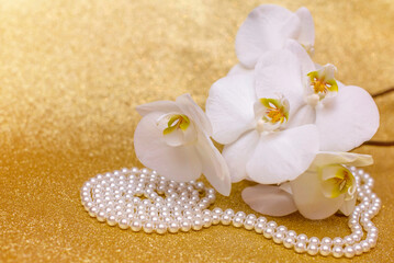 Fototapeta na wymiar white Orchid and pearl necklace on a shiny gold background 