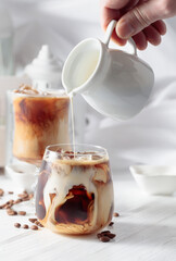 Cream is poured into a glass with iced coffee.