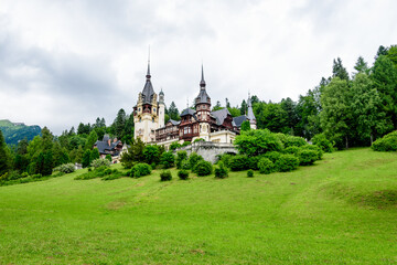 Beautiful neo-Renaissance building of Peles Castle (Castelul Peles) near Bucegi Mountains (Muntii Bucegi) in a cloudy summer day in Sinaia town, Romania .
